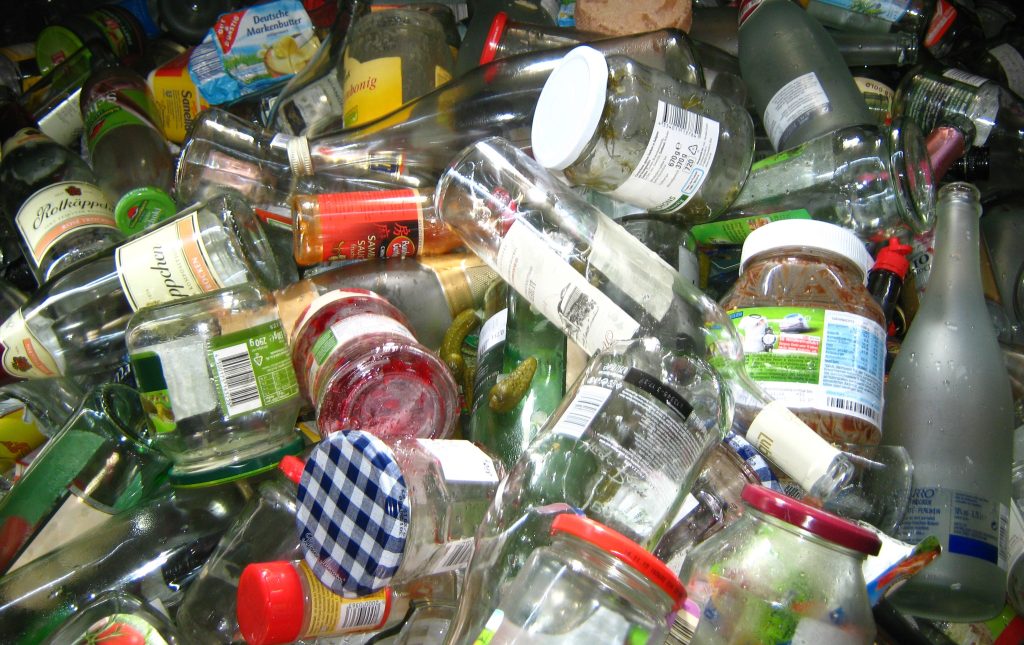 A imagem apresenta diversos resíduos sólidos empilhados, incluindo garrafas de vidro, potes de geleia e molho.